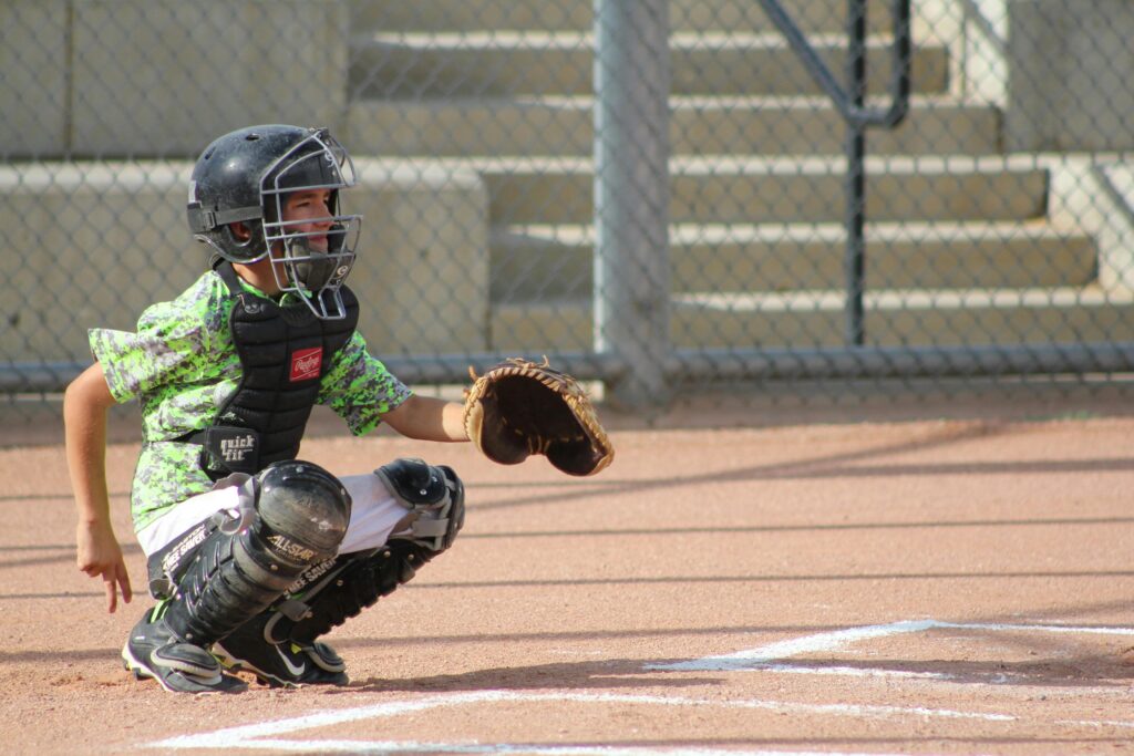 A high school baseball catcher crouching on the field and giving hand signals, representing game strategy and the state of the game analysis.